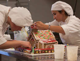 Two culinary students decorate a gingerbread house