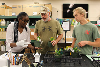 Three horticulture students stand at a table with plants