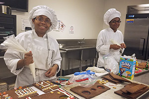 two culinary students working on gingerbread houses