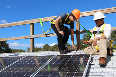 two people install solar panels on a roof