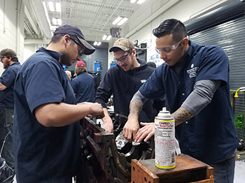 three students work on a diesel engine