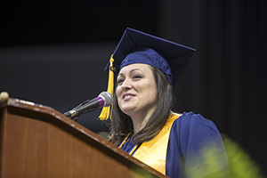 woman in cap and gown speaks at podium