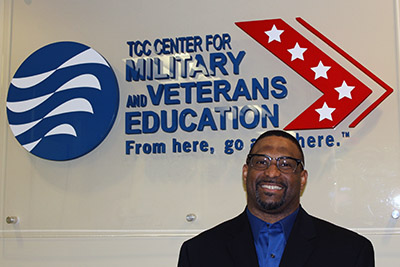 Smiling man standing in front of the logo for TCC's Center for Military and Veterans Education