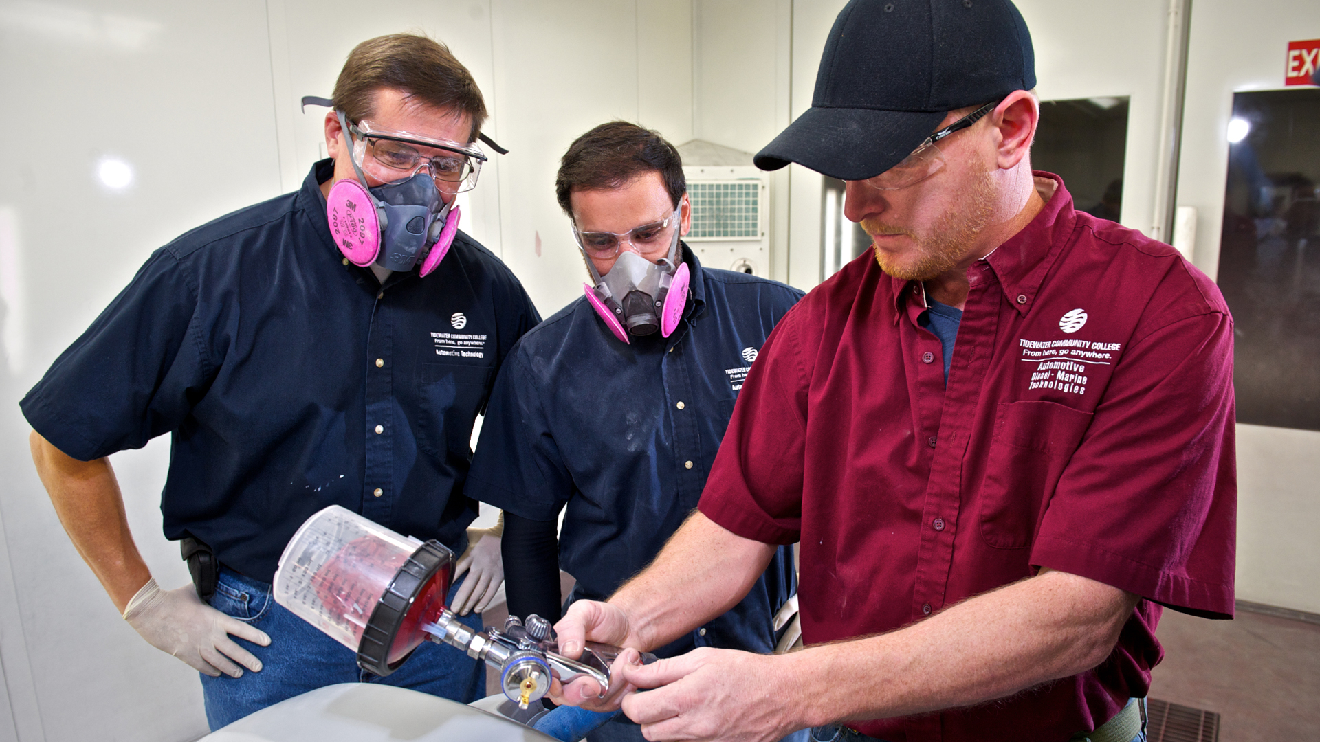 instructor and two automotive students working on a car